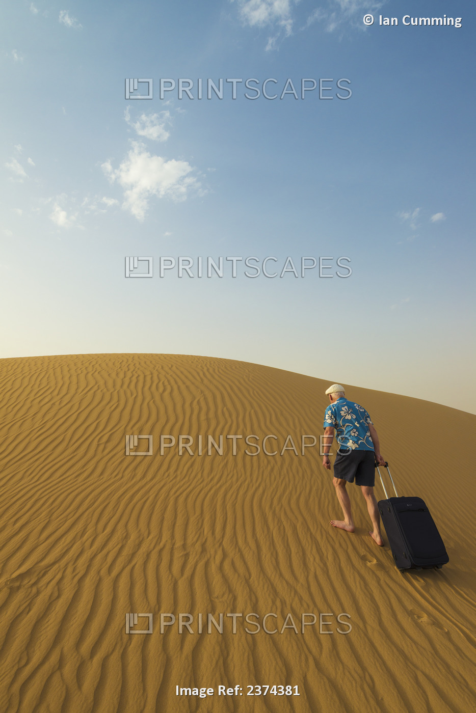 Barefoot Man With Suitcase Walking Up Sand Dune; Dubai, United Arab Emirates