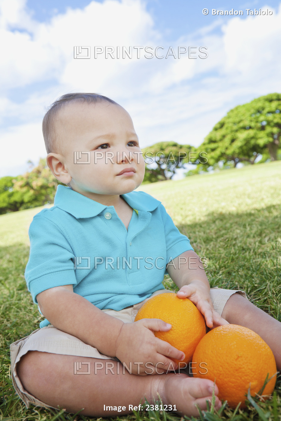 Young Boy Sitting On The Grass At A Park With Oranges; Honolulu, Oahu, Hawaii, ...