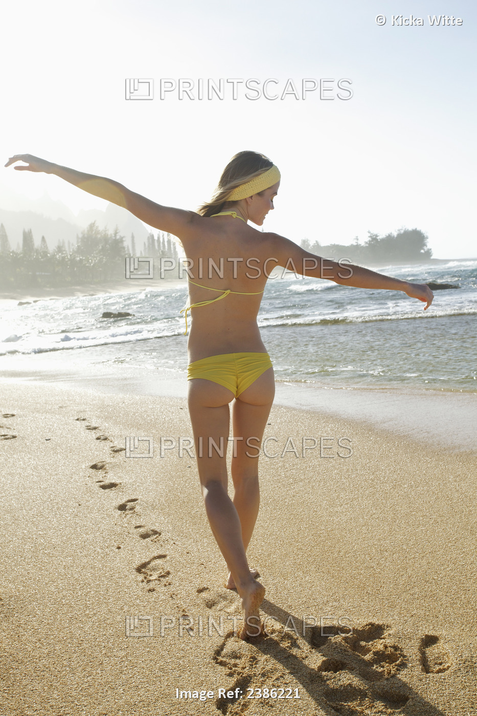 A Young Woman In A Yellow Bikini Walks On The Wet Beach Along The Water's Edge; ...