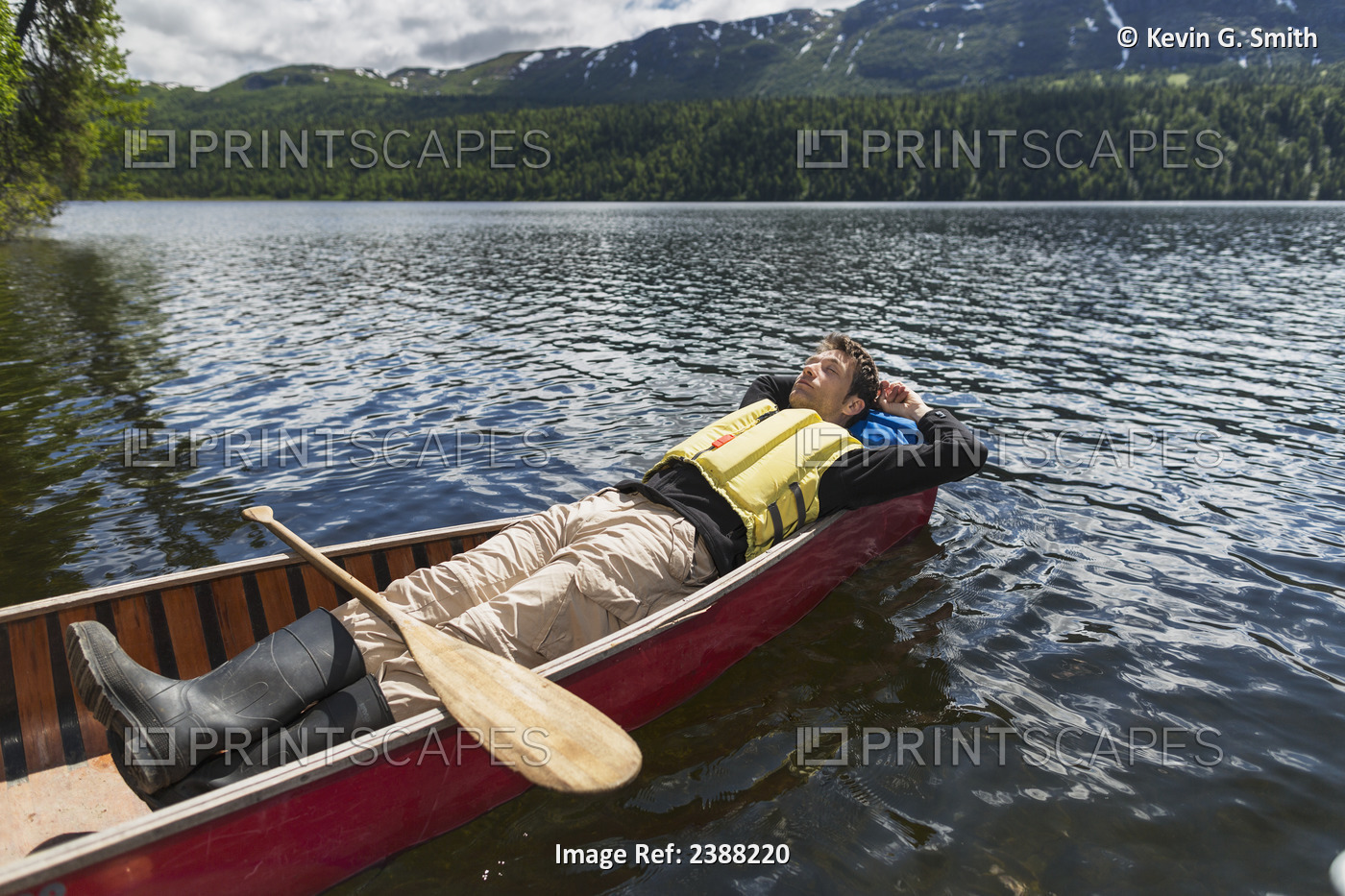 Man Reclined In Canoe And Resting In The Sunshine On Byers Lake With Forested ...