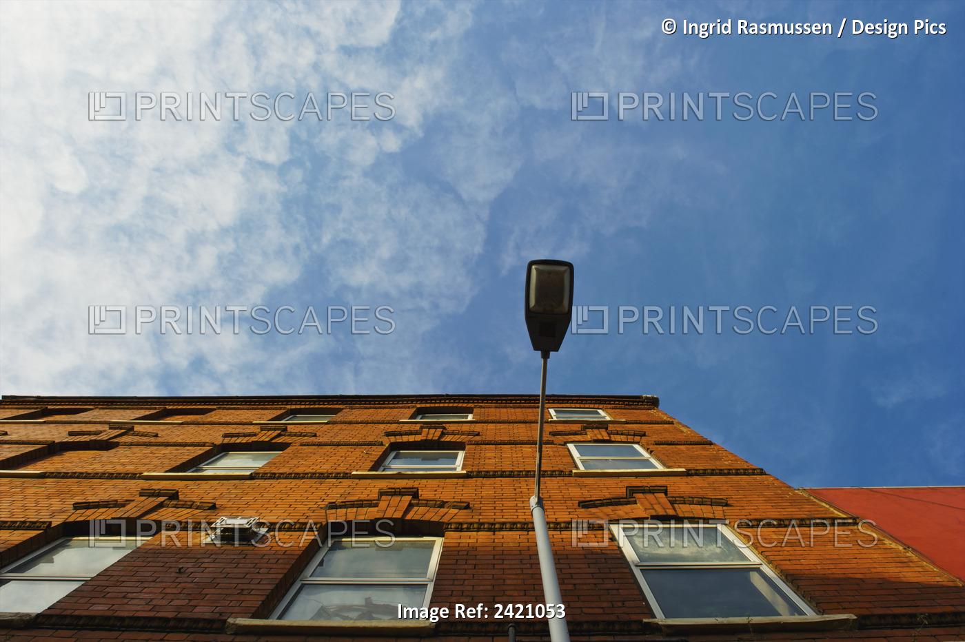 Low Angle View Of A Brick Building And Street Light With Blue Sky And Cloud; ...