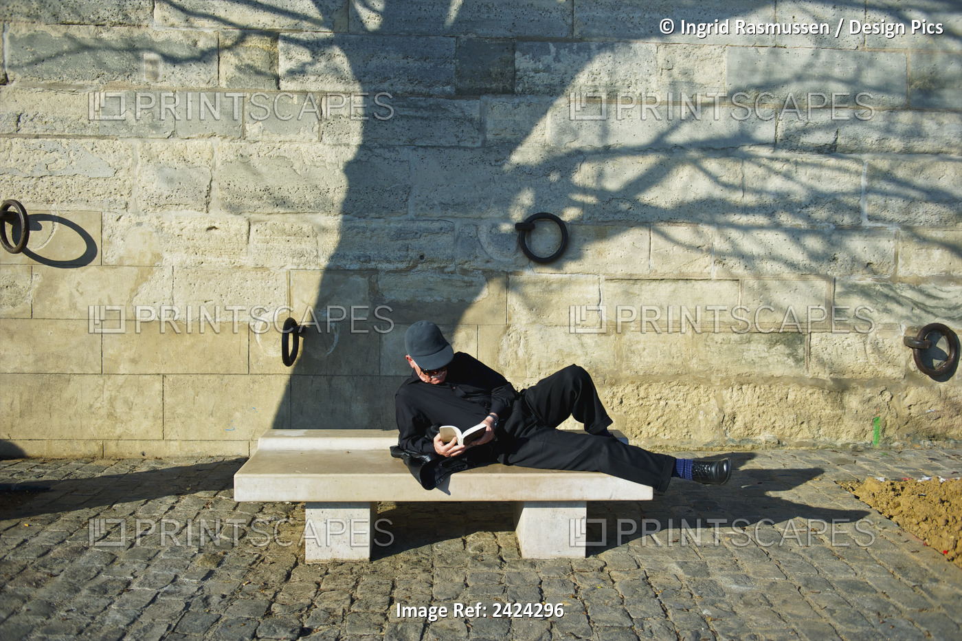 A Man Lays Across A Bench Reading A Book; Paris, France