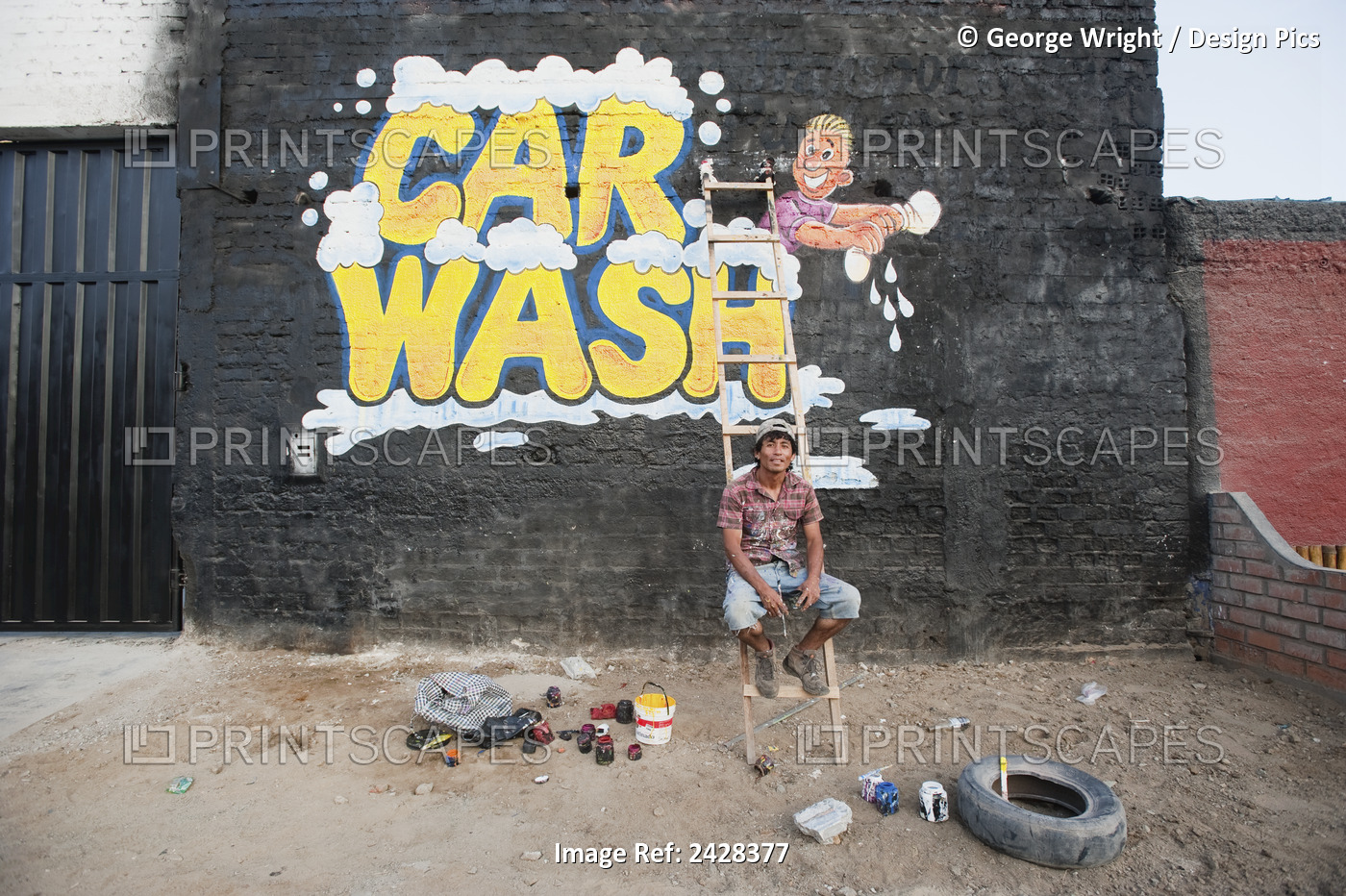 A Man Sits On A Ladder In Front Of His Painted Car Wash Sign On A Brick Wall; ...