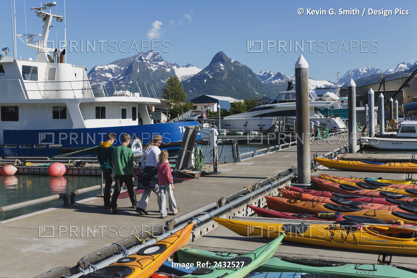 Family Walks On The Dock Past Multi Colored Kayaks With Harbor And Mountains In ...