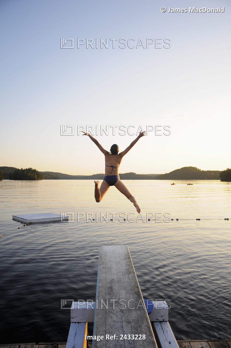 A Swimmer Jumps Off A Diving Board As The Sun Sets Over A Lake In Muskoka; ...