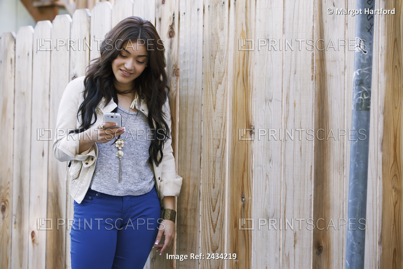 A Woman Leaning Against A Wooden Fence Using Her Cell Phone; San Francisco, ...