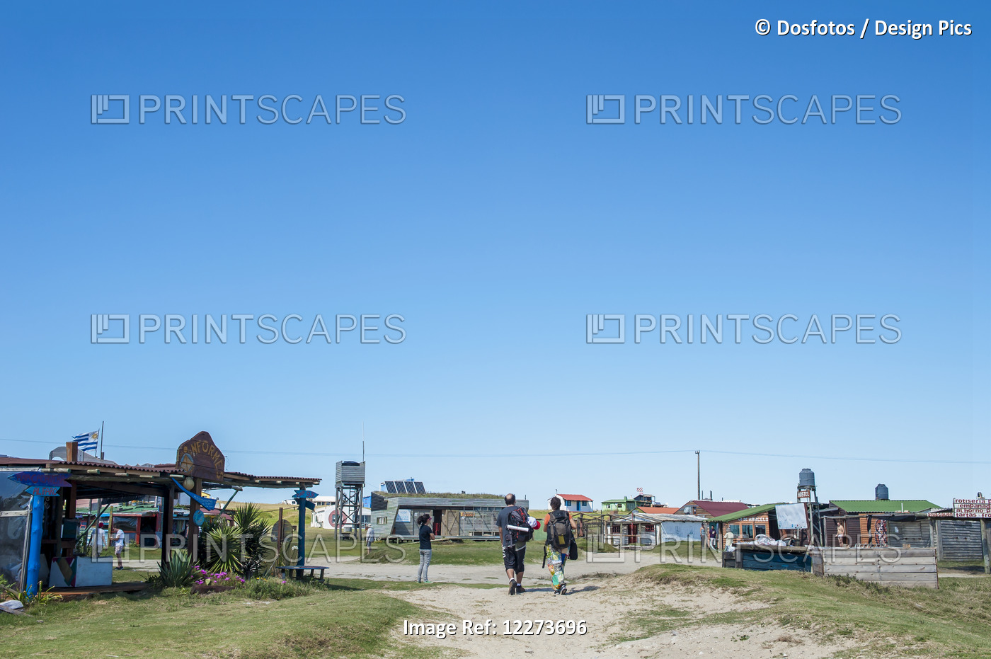 Pedestrians Walking On The Sandy Path By Buildings And Hostels On The Coast; ...