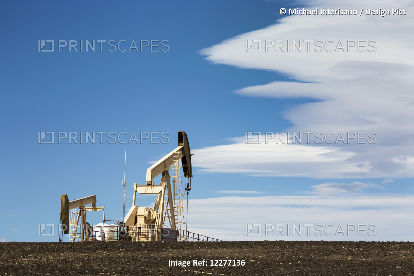 Two Pumpjacks On A Hill With Dramatic Clouds In The Blue Sky; Alberta, Canada