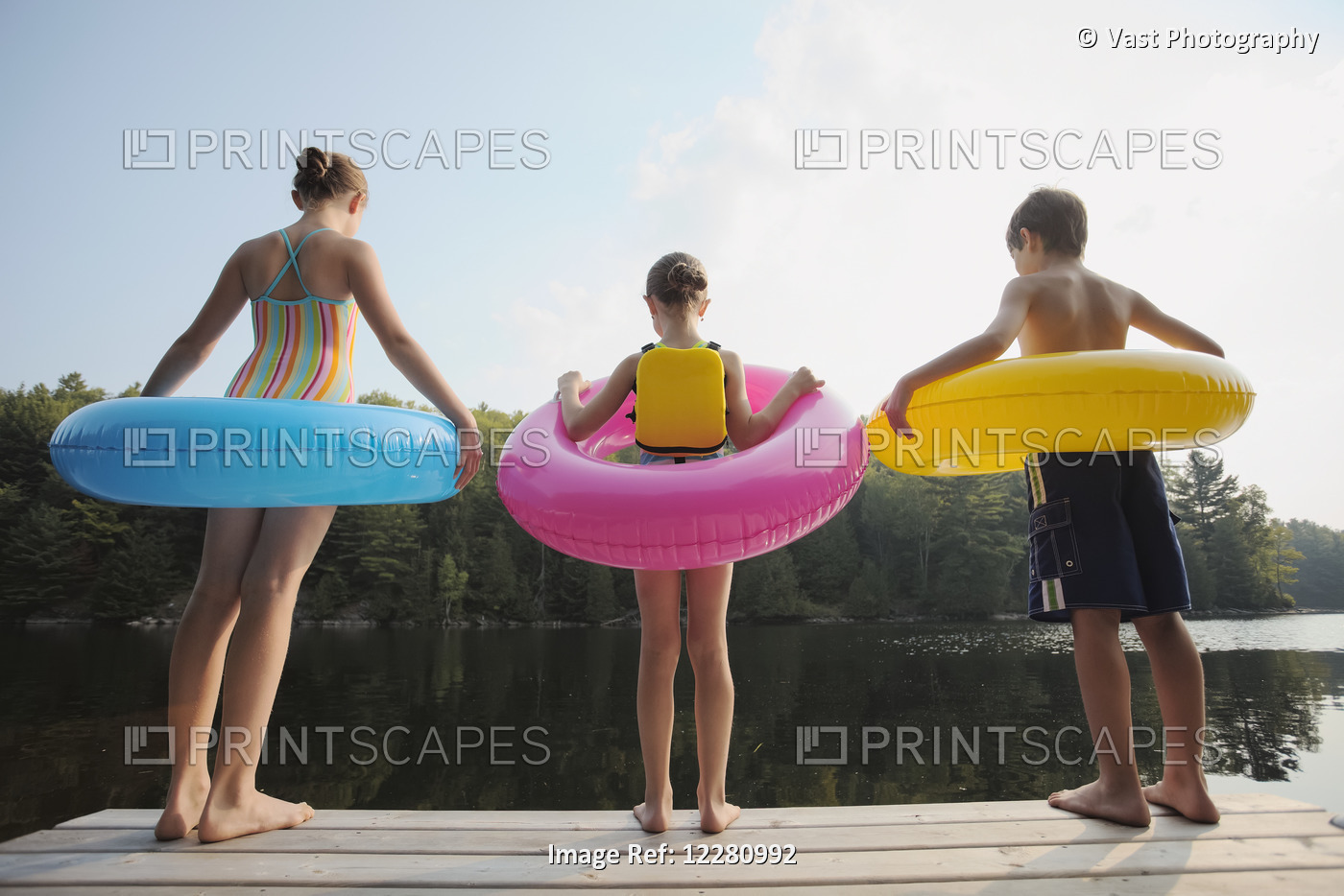 Kids Standing At End Of Dock Holding Inflatable Rings On Crystal Lake; Ontario, ...