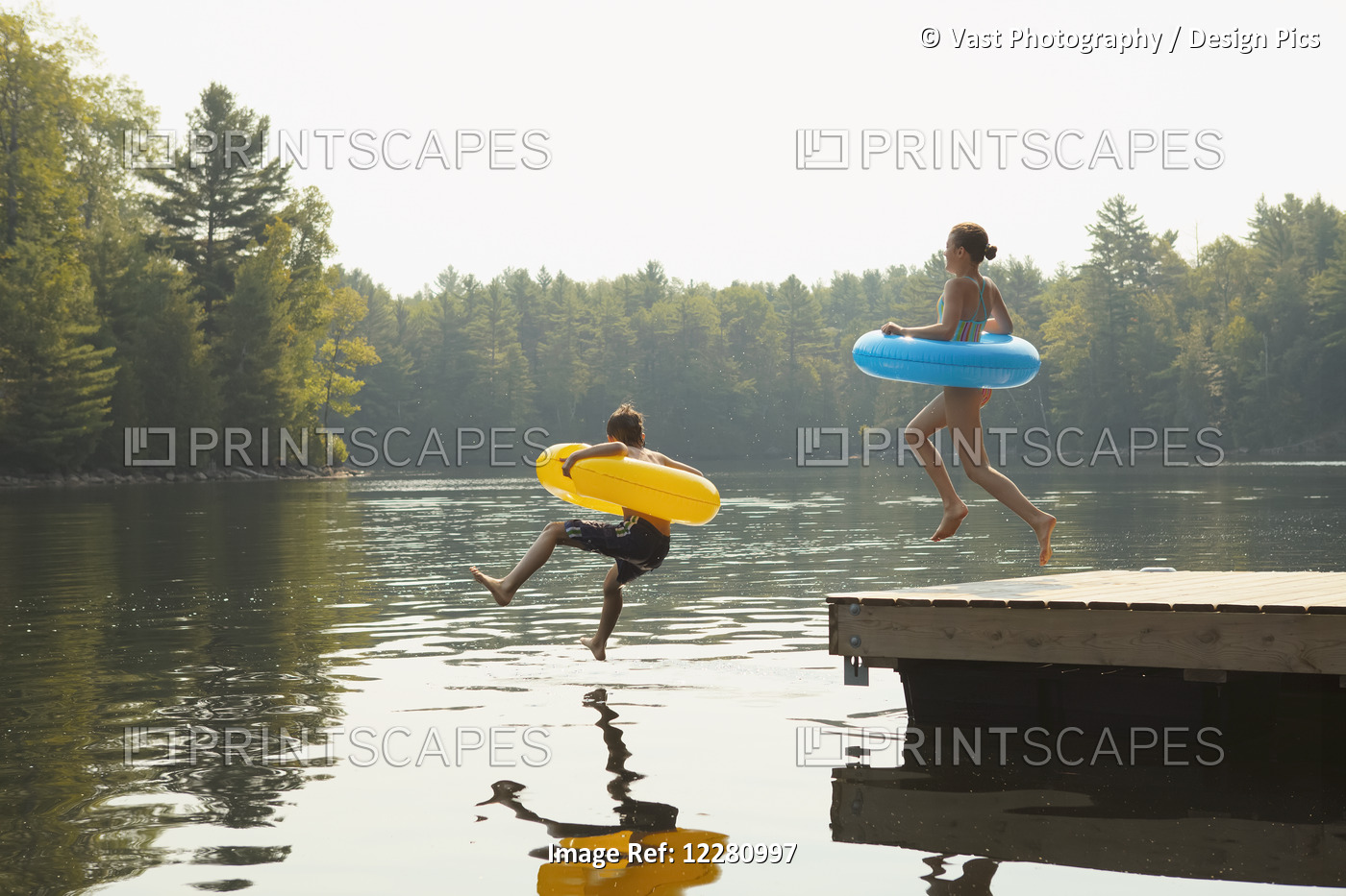 Kids Jumping Off End Of Dock Holding Inflatable Rings On Crystal Lake; Ontario, ...