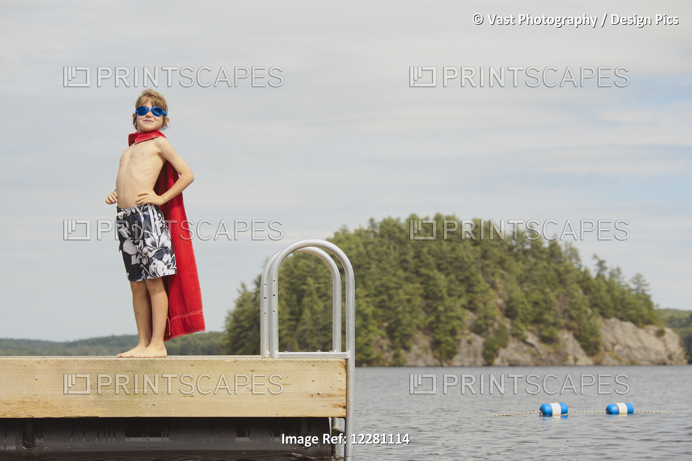 Boy Standing On Dock Wearing Goggles And Towel Pretending To Be A Super Hero; ...