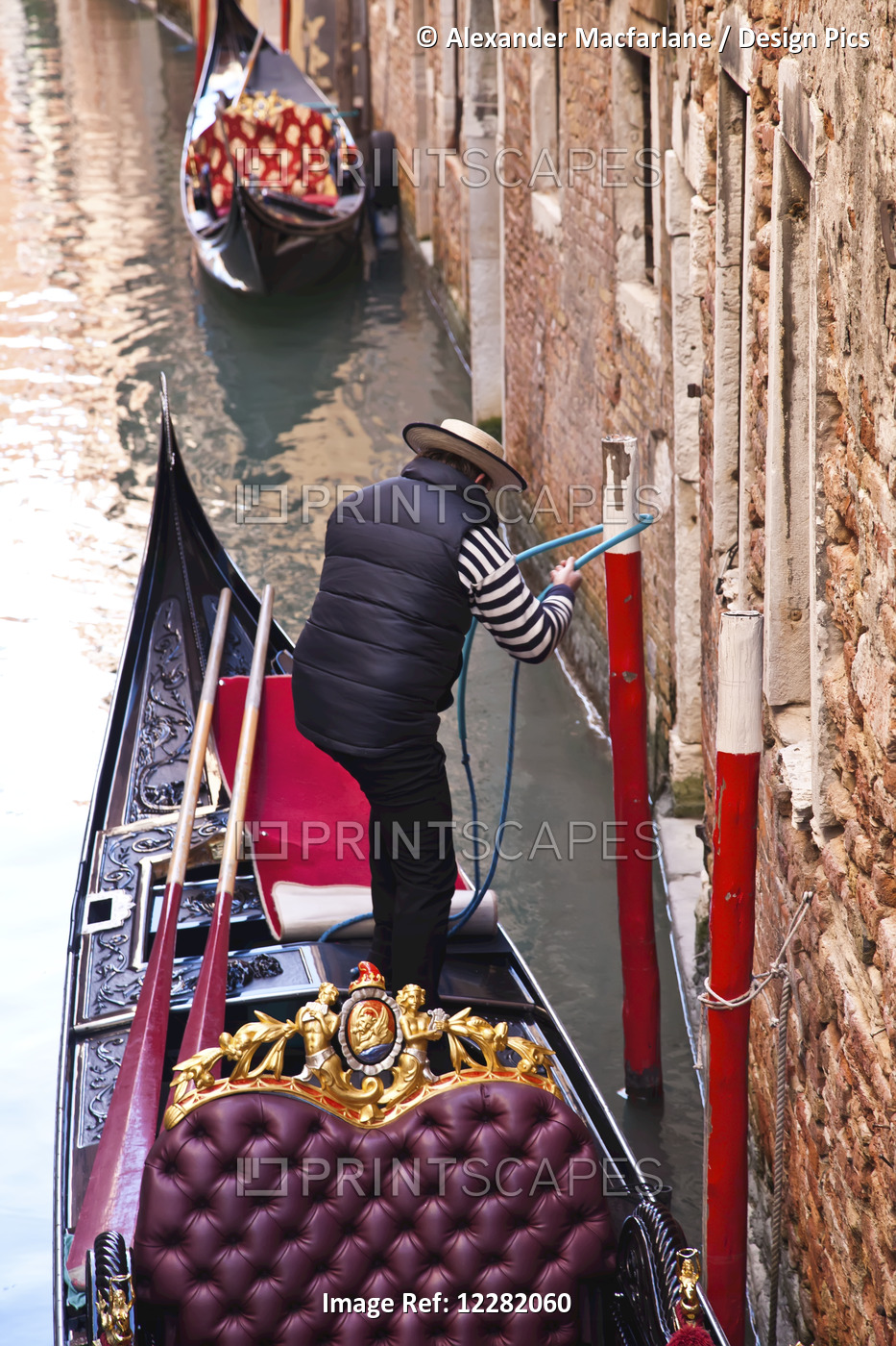 Gondolier Tying His Gondola To A Post Beside A Building On A Canal; Venice, ...