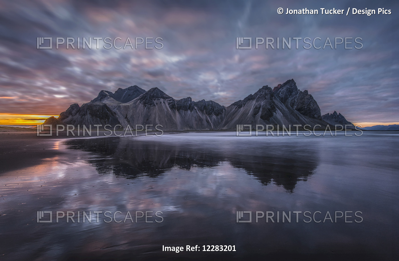 Rugged Mountain Peaks And A Colourful Sunset Reflected In Tranquil Water; ...