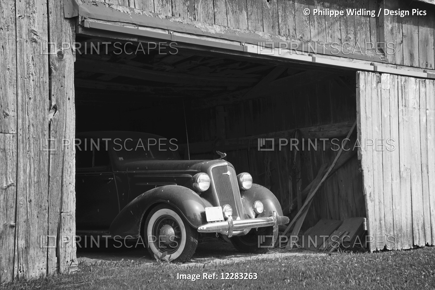 Black And White Image Of The Front Of An Antique Car Inside A Wooden Barn; ...