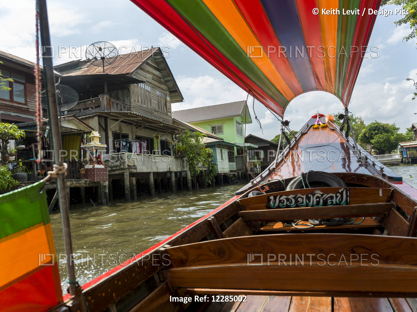 A Boat On The River With A Colourful Cover And Houses Along The Shoreline; ...