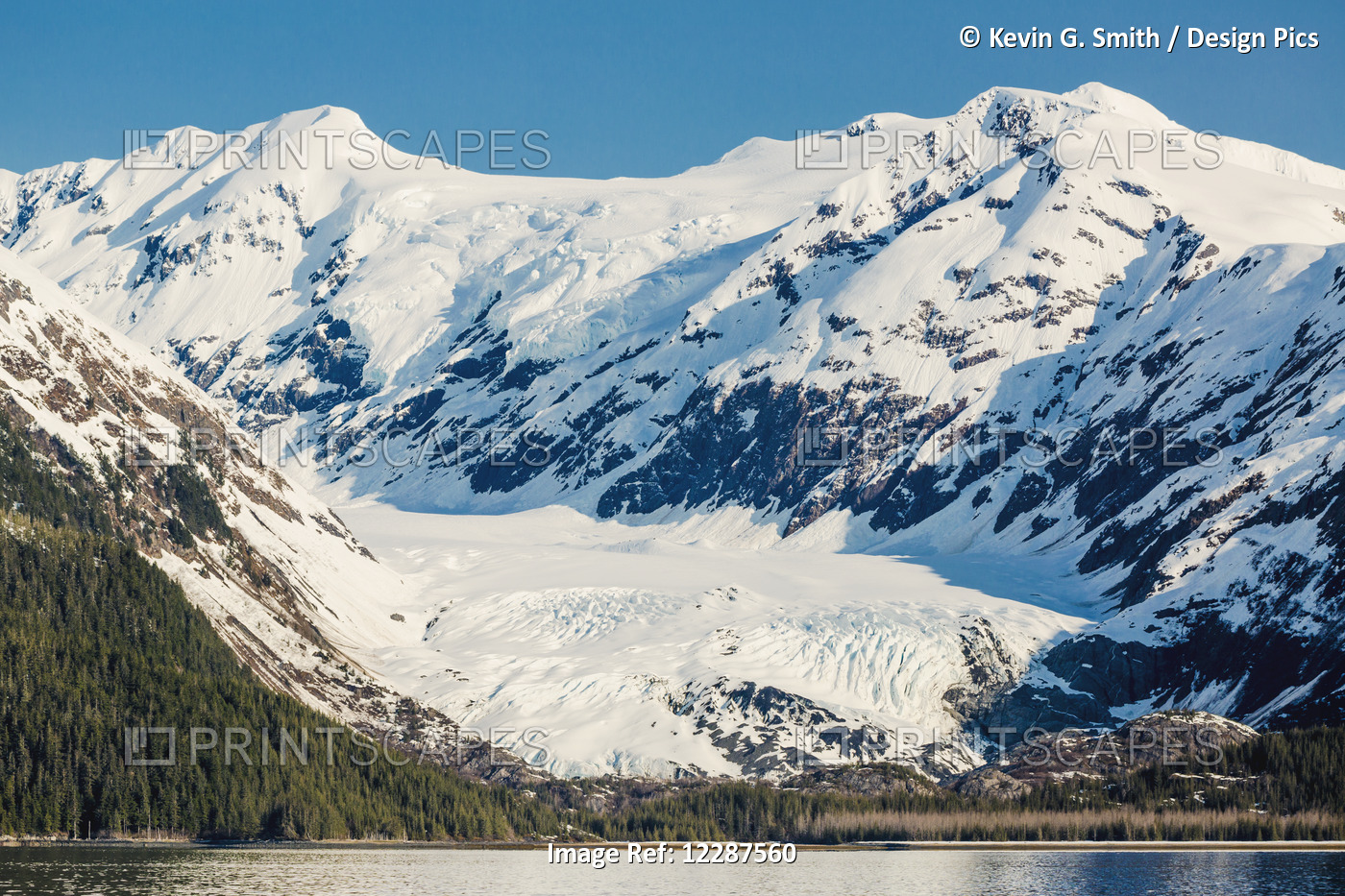 A Glacier Sits In The Valley Of Snow Covered Mountains Above Hillsides Of ...