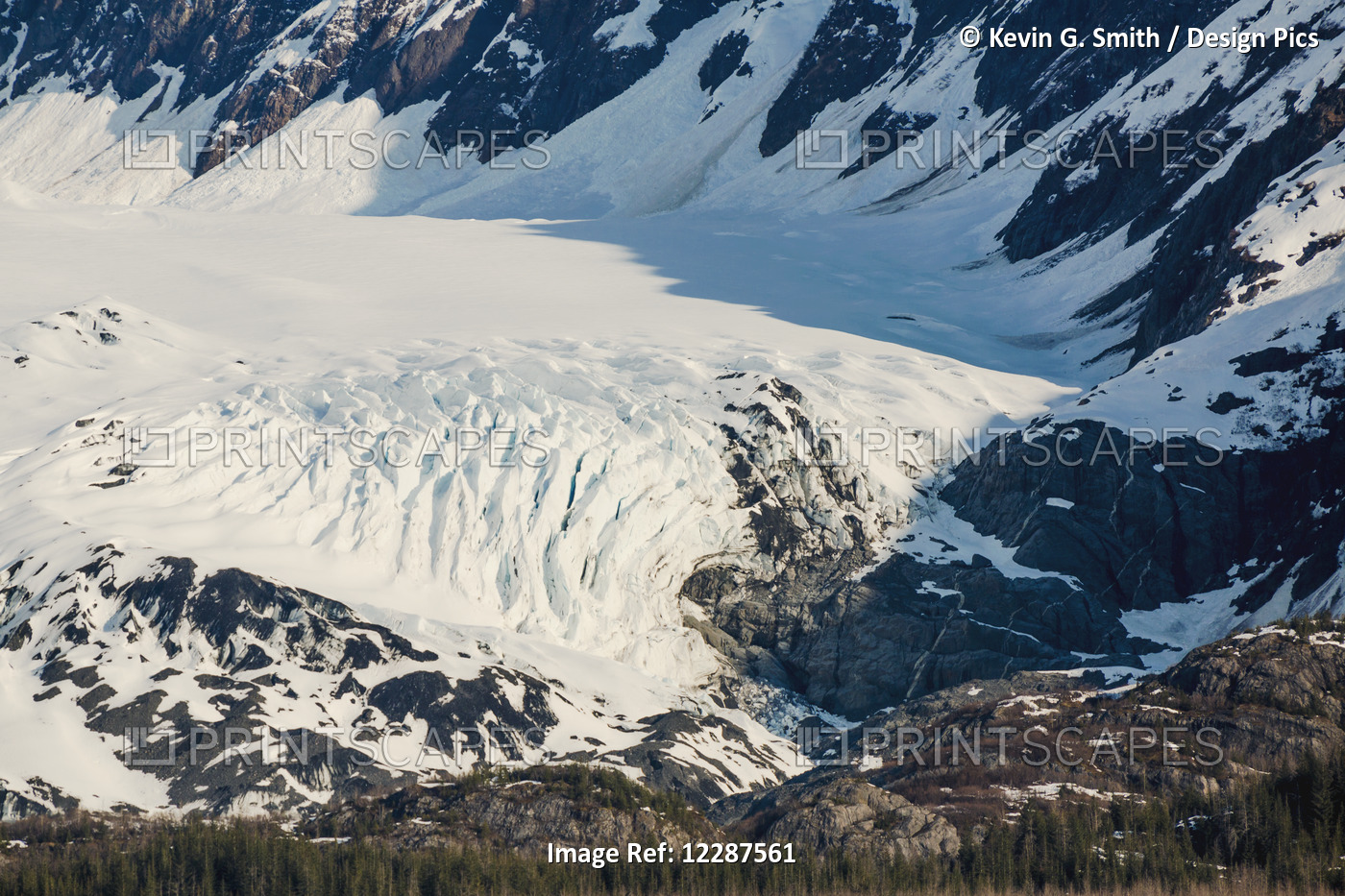 A Glacier Sits In The Valley Of Snow Covered Mountains Above Hillsides Of ...