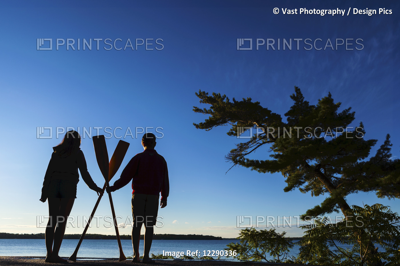 Boy And Girl Holding Paddles Overlooking Balsam Lake At Sunrise; Ontario, Canada