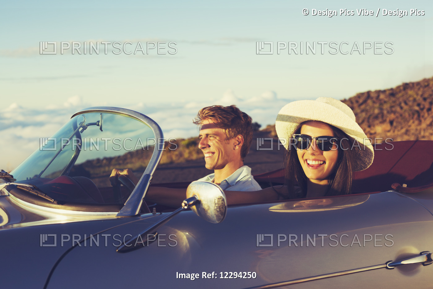 Happy Young Couple In Classic Vintage Sports Car At Sunset