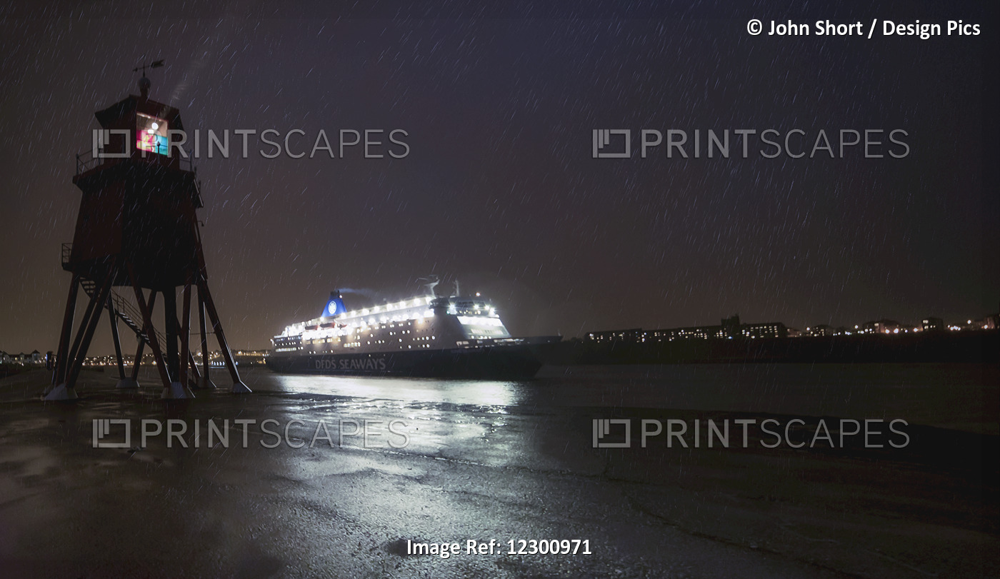 Light Streaming From A Lighthouse On The Coast As An Illuminated Cruise Ship ...