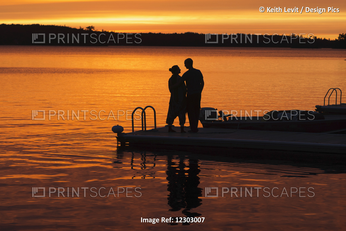 Silhouette Of A Couple Standing At The End Of A Dock At Sunset With An Orange ...