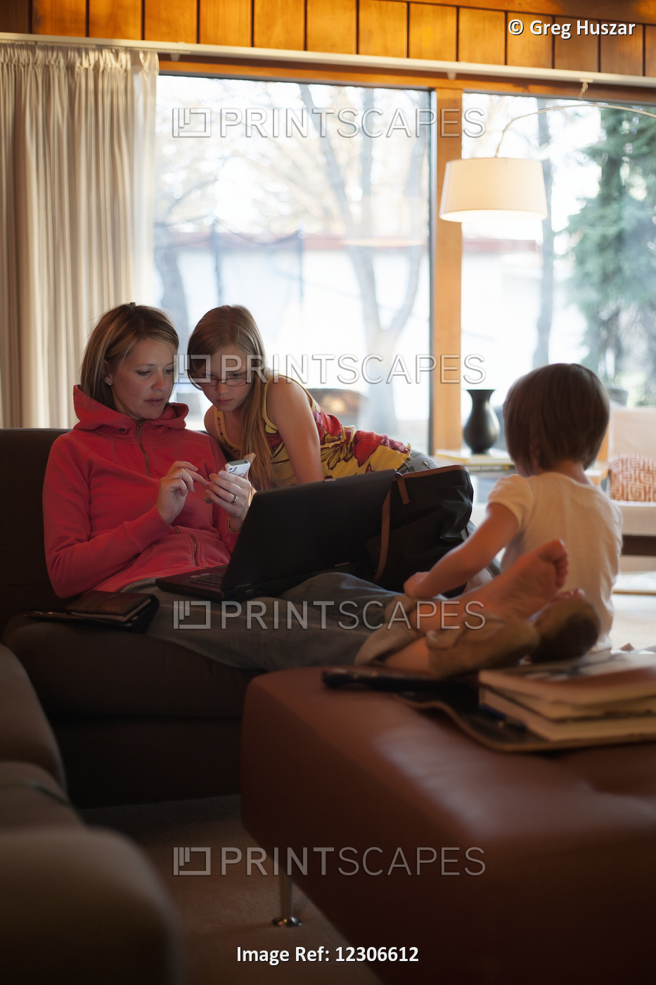 Mother At Home With Daughters Using Mobile Phone And Laptop; Regina, ...