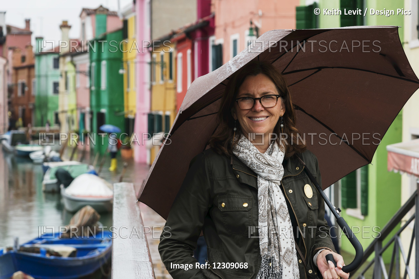 A Woman Stands Beside A Canal With An Umbrella With Colourful Houses In A Row ...