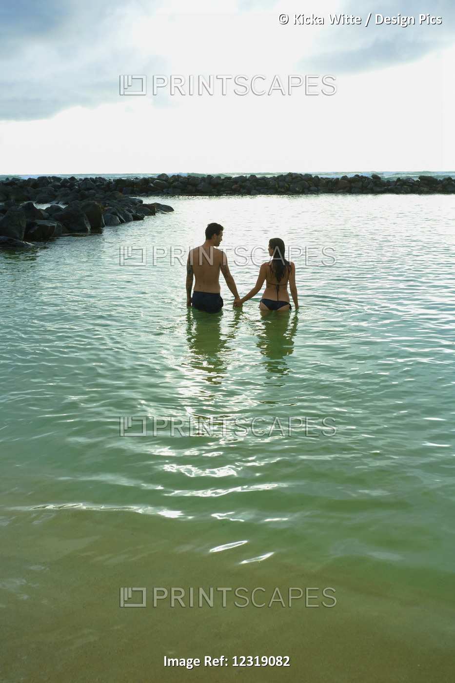 A Couple Holds Hands And Walks Into The Ocean Off Lydgate Beach; Kauai, Hawaii, ...