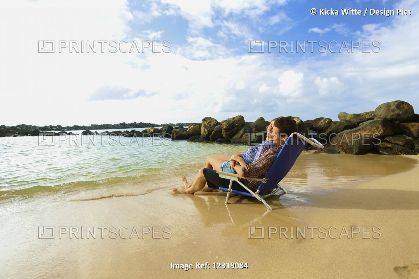 A Couple Sits In A Beach Chair Together Facing The Ocean On Lydgate Beach; ...