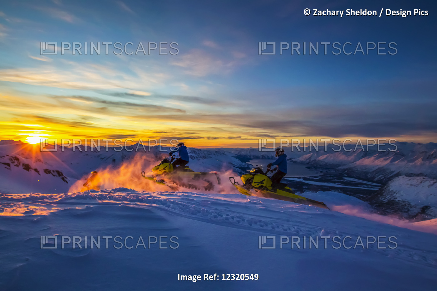 Two Men On Snowmobiles Ride Off Towards The Sunset With Valdez In The ...