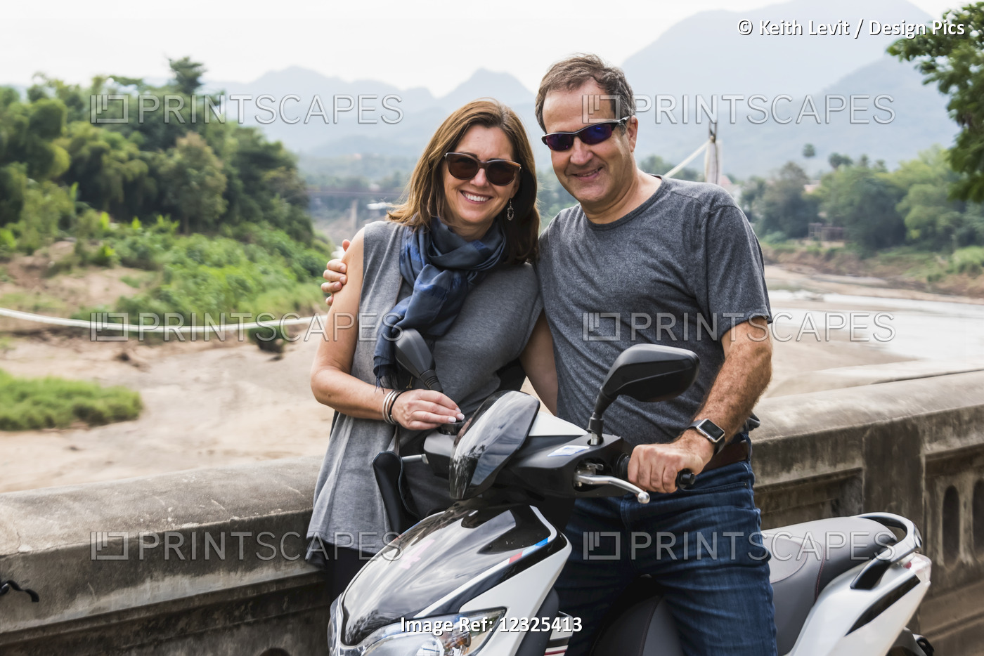 A Couple Stand Posing By A Motorcycle With A Mountainous Landscape In The ...