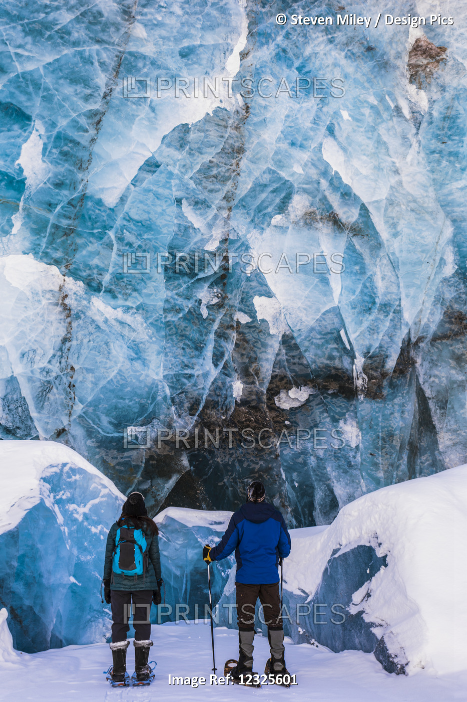 A Couple Of Snowshoers Examine A Large Blue Wall Of Ice With Several Collapsed ...