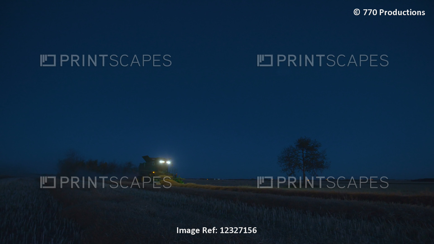 A combine working at night picking up swaths during a Canola harvest and a ...