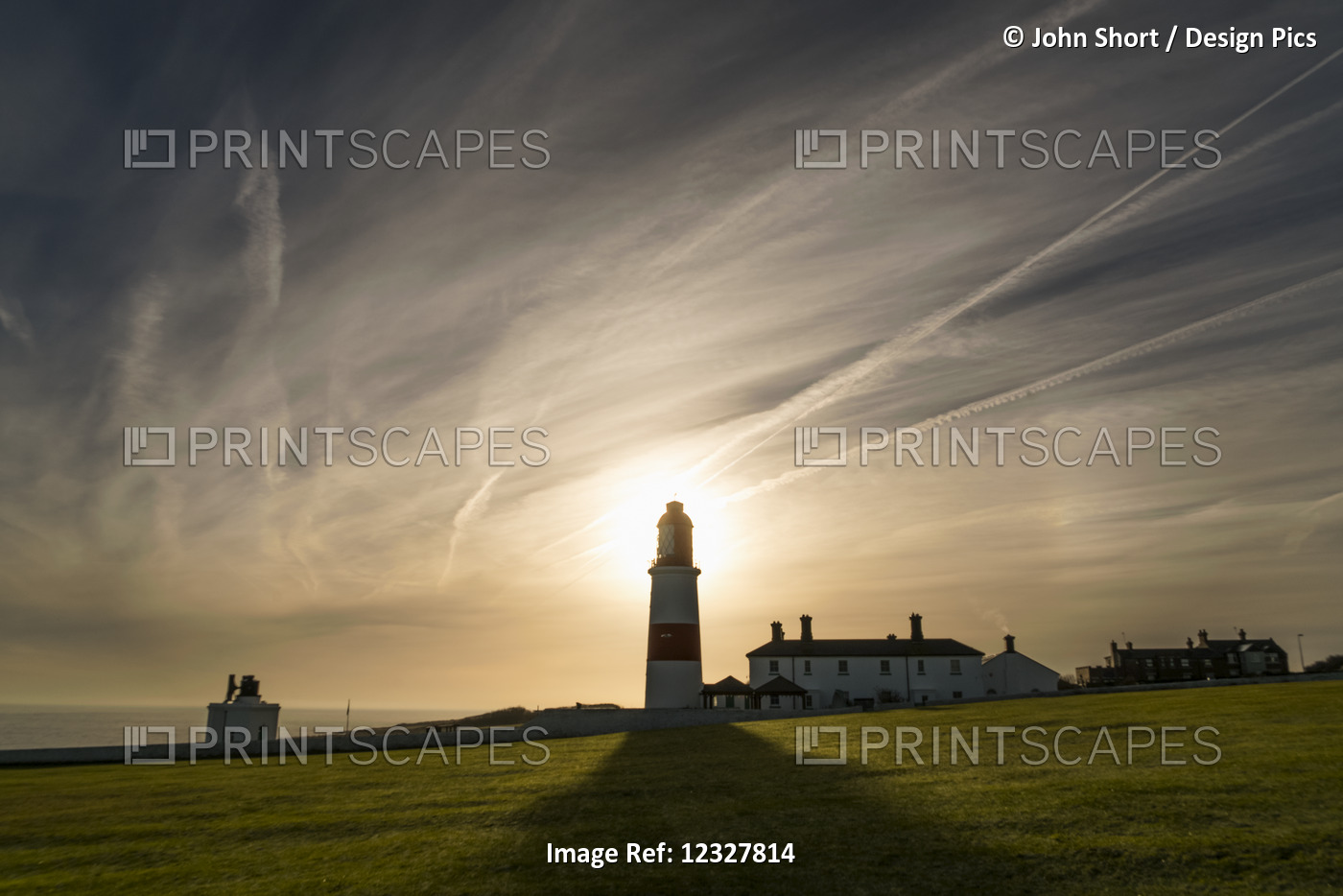 Sunlight Behind A Lighthouse Casts A Shadow On A Grass Field Along The Coast; ...