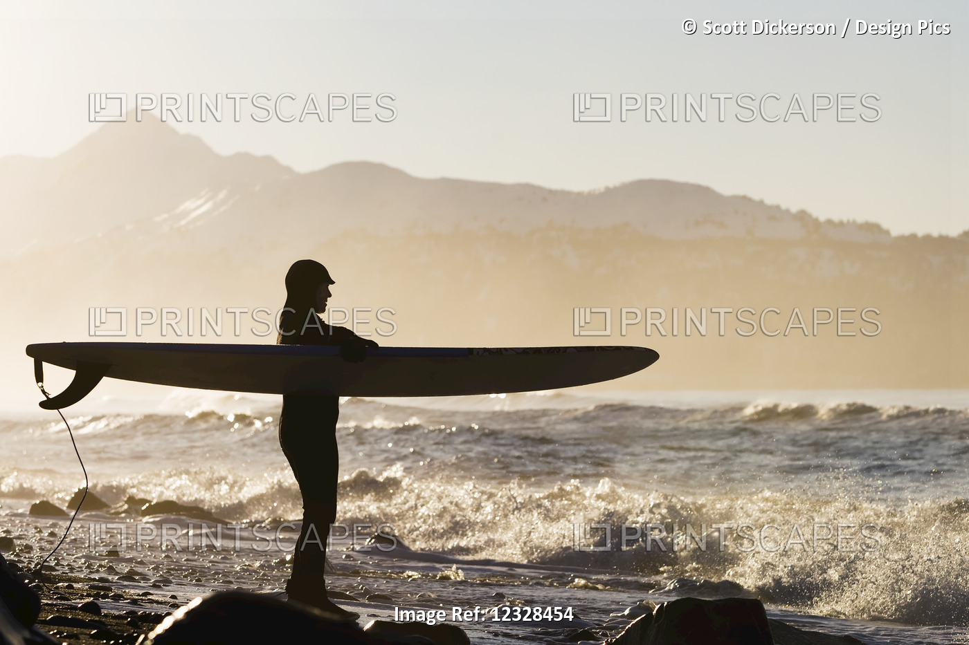 Female surfer standing along the wet shore of Kachemak Bay, South-central ...