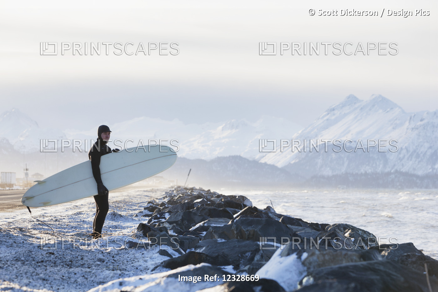 Surfer with surfboard looking out over Kachemak Bay, South-central Alaska; ...