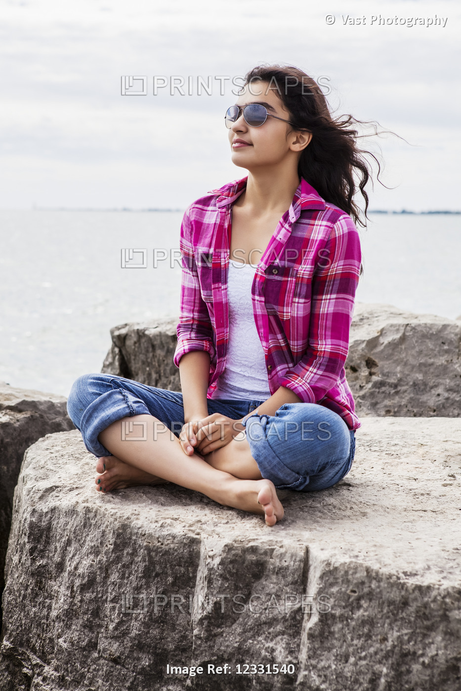 Teenage girl sitting on rocks looking out at the lake, Woodbine Beach; Toronto, ...