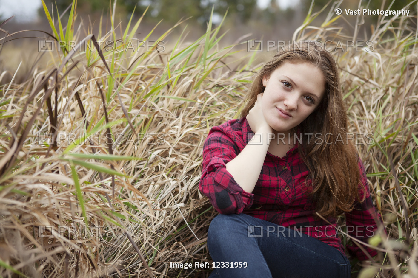Portrait of a girl sitting in a field of tall grass looking at the camera; ...
