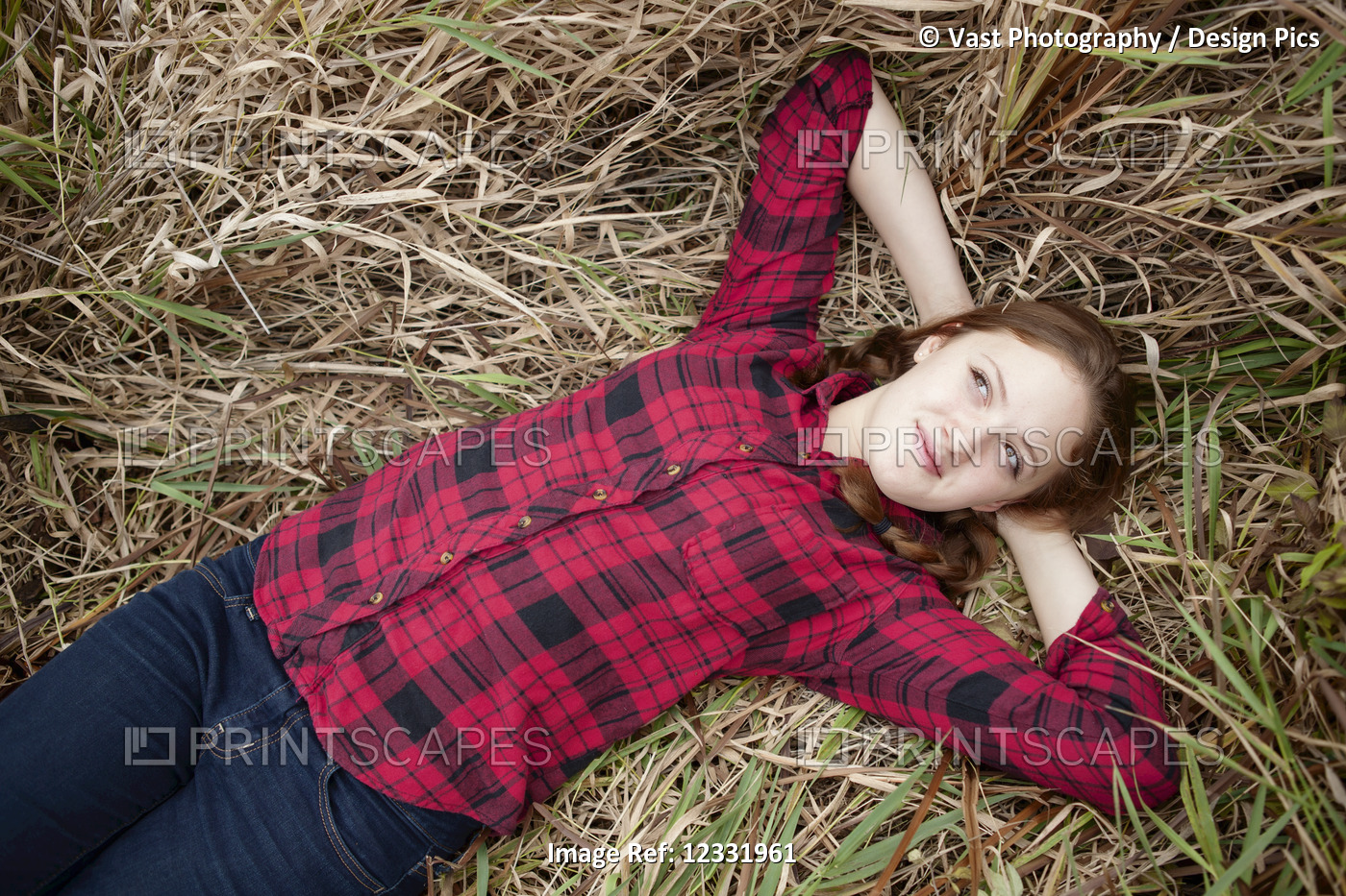 Portrait of a girl lying in a field of tall grass looking up; Toronto, Ontario, ...