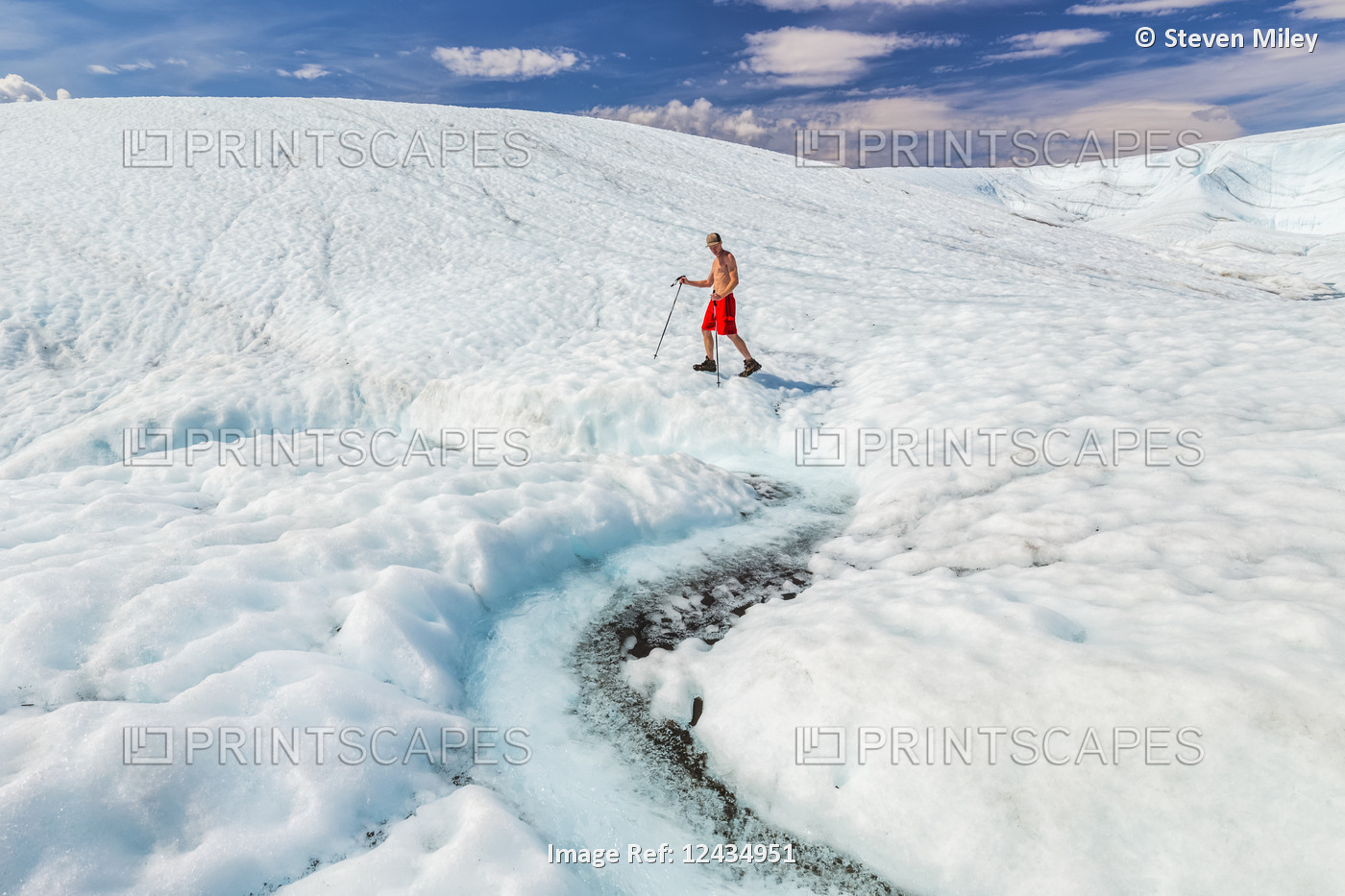 A shirtless man in a bathing suit walks across the surface of Root Glacier with ...