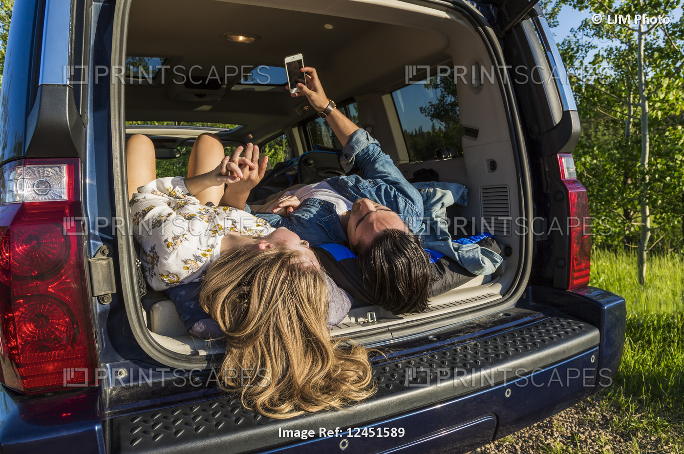 Young couple laying in the back of their packed vehicle on a road trip, showing ...