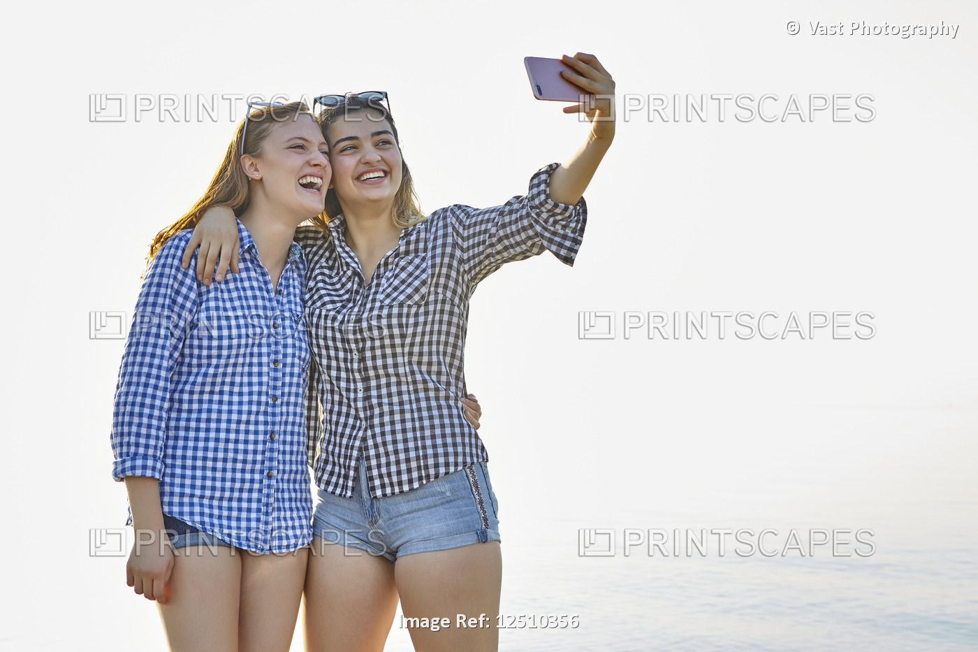 Two teenage girls take a self-portrait as they stand in an embrace at sunset at ...