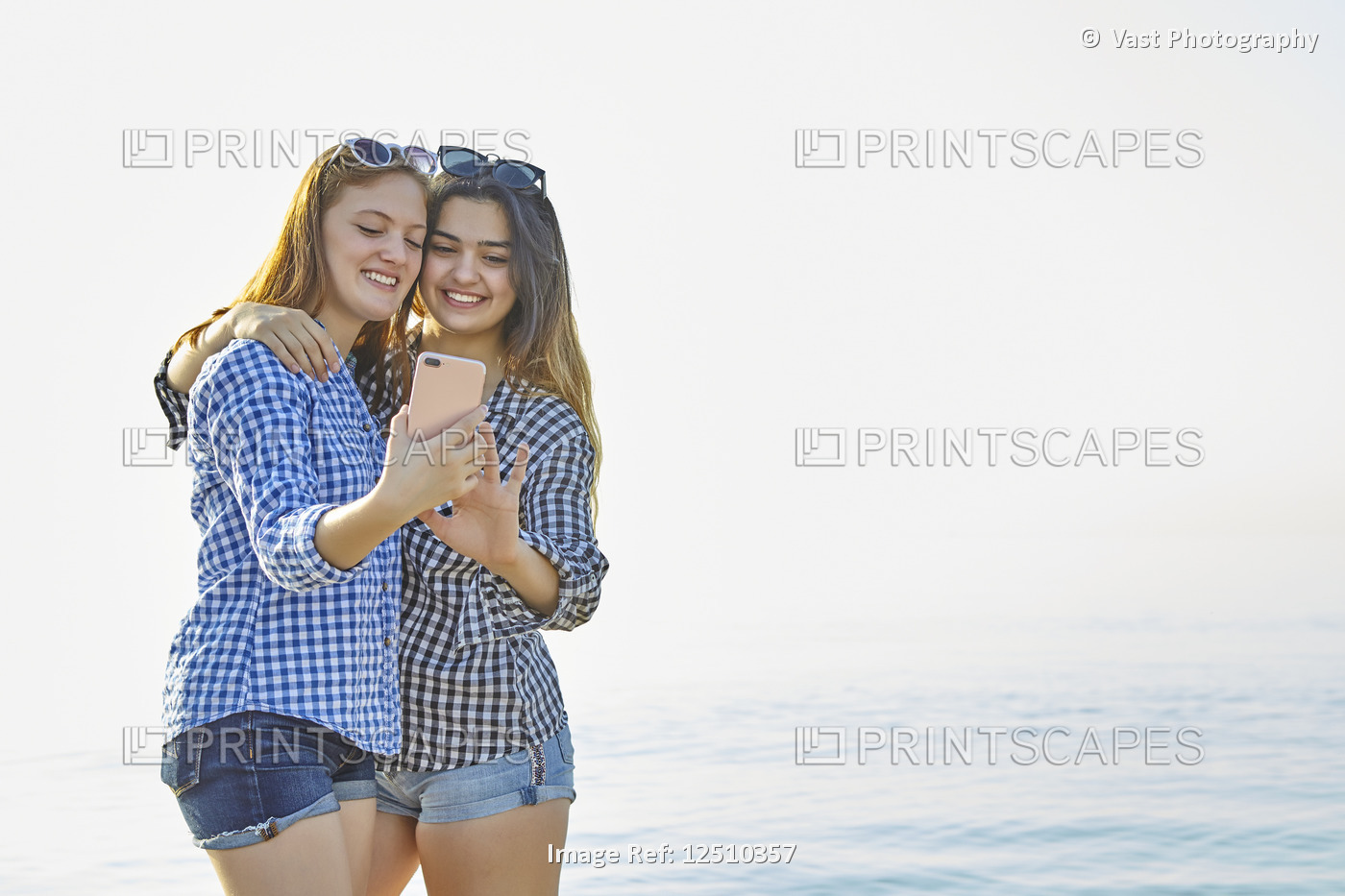 Two teenage girls take a self-portrait as they stand in an embrace at sunset at ...