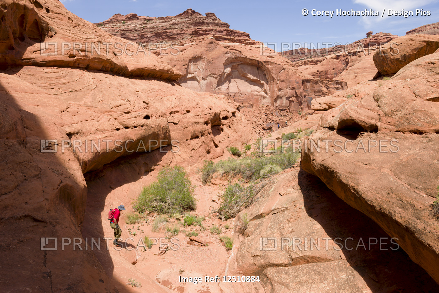 Man crossing a desert canyon with team in distant background walking a trail ...
