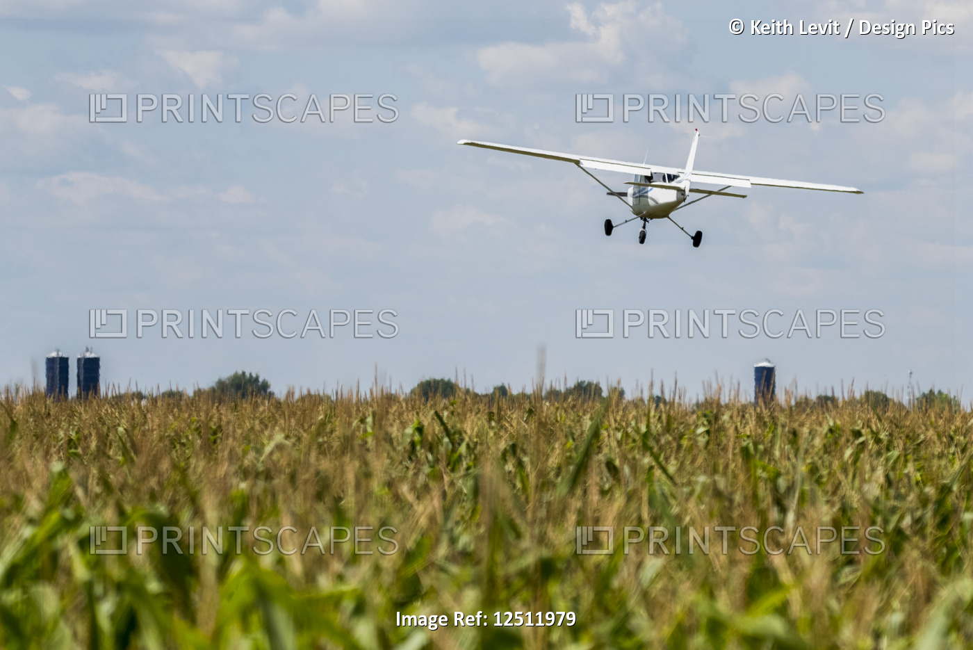 A small plane flies low over a farm field; Manitoba, Canada