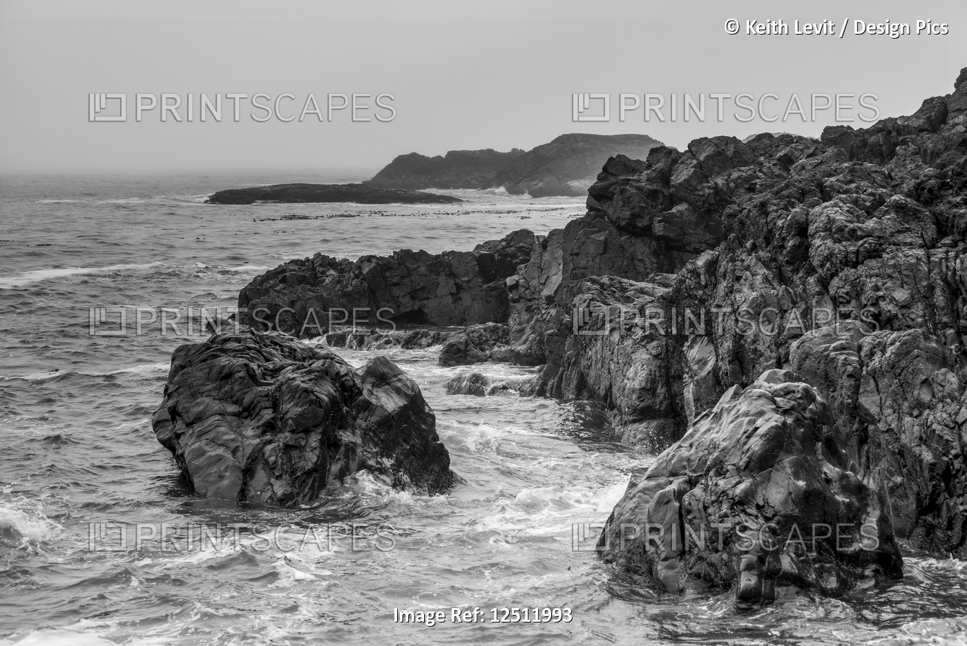 Rugged rocks line the coast at Chesterman Beach with clouds and mist obscuring ...