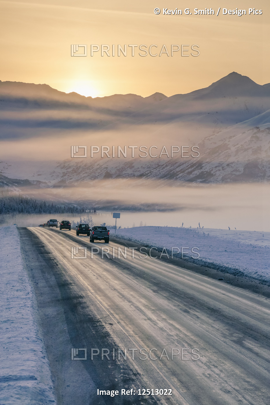 A foggy sunset illuminates cars driving down a snow-covered Seward Highway, the ...