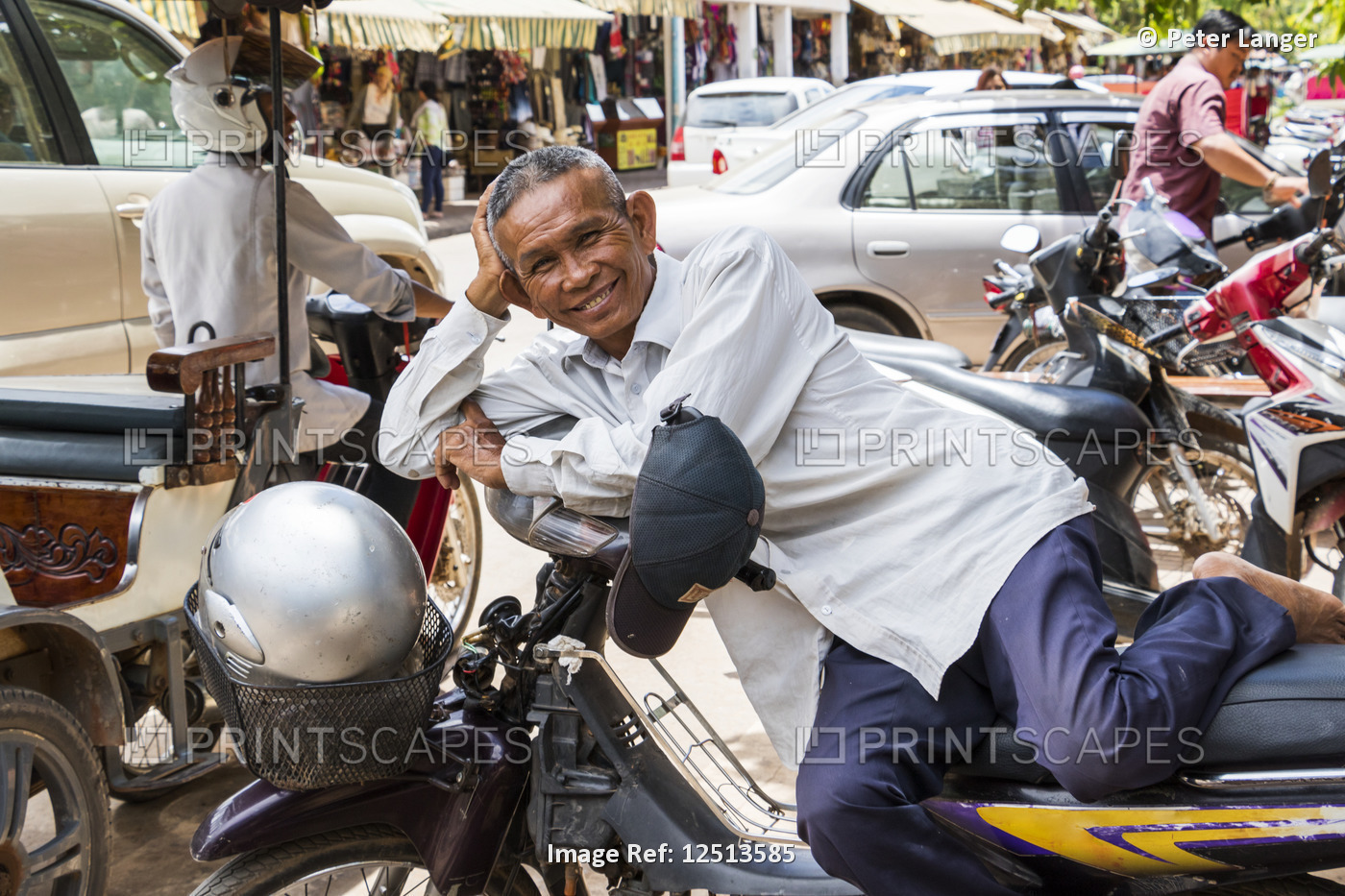 Cambodian man resting on a motorcycle; Siem Reap, Cambodia