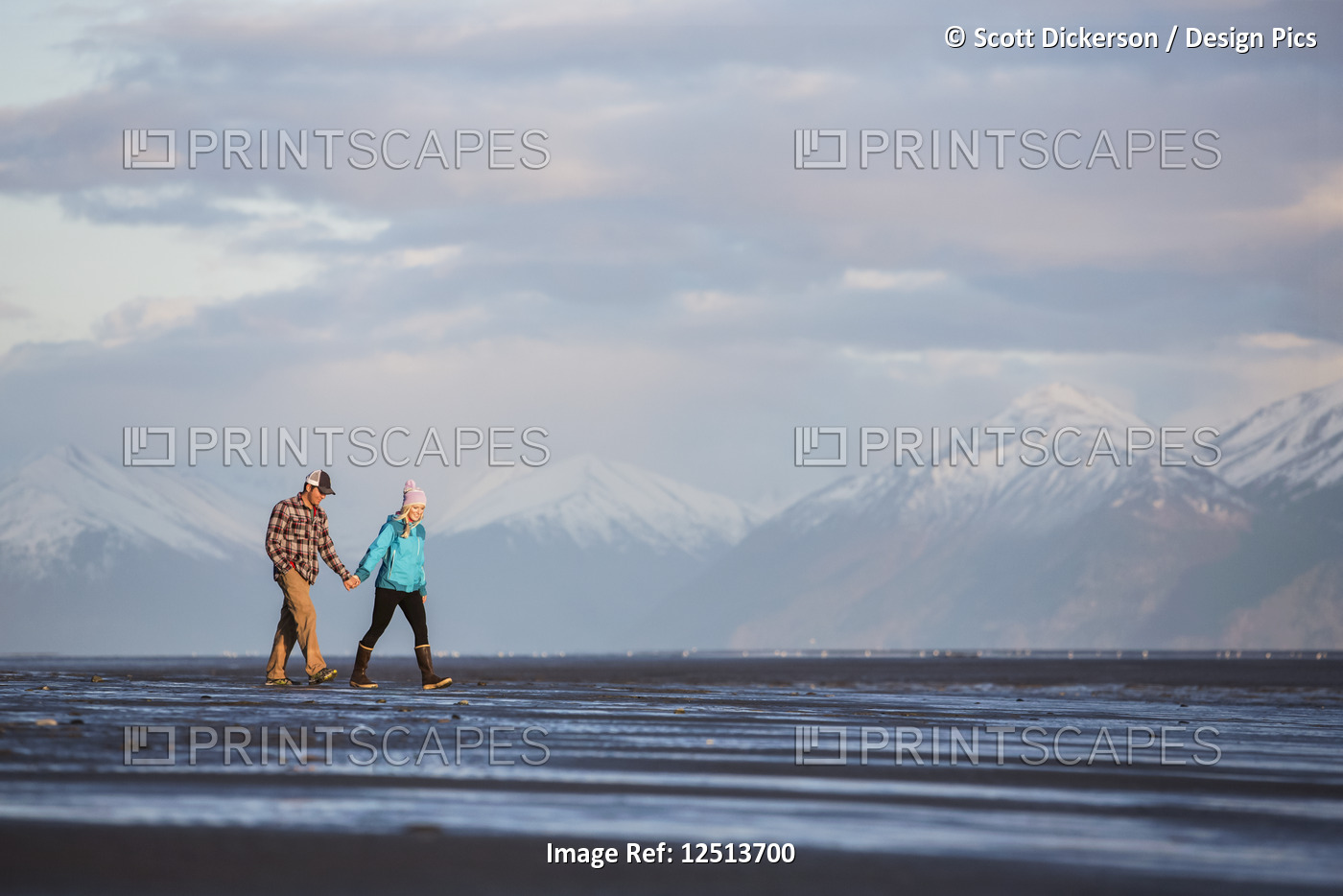 A young couple walking on a beach and holding hands with a mountain range in ...