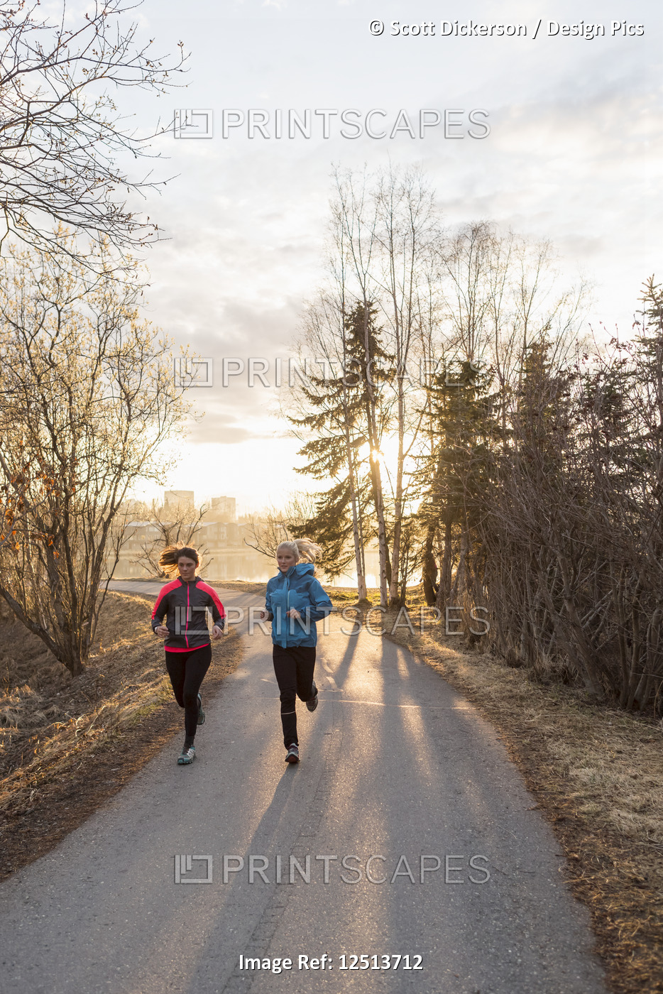 Two young women running on a trail at sunrise; Anchorage, Alaska, United States ...